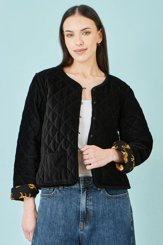 A woman modeling a black quilted cropped jacket with Leopard patterned cuffs, worn over a white top and blue jeans, against a solid light blue background.